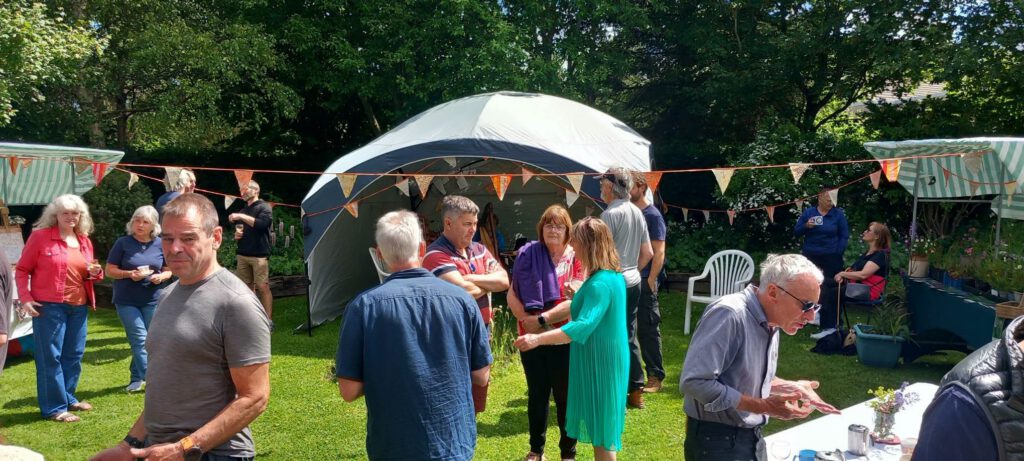 A summer garden party in progress with various stalls.