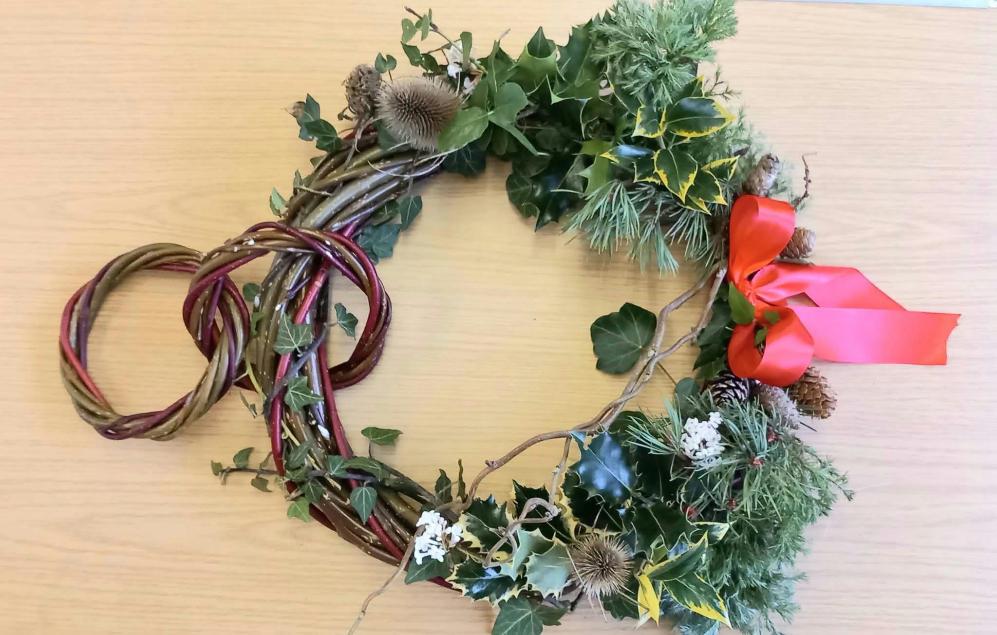 A natural willow Christmas wreath sitting on a light wooden surface.